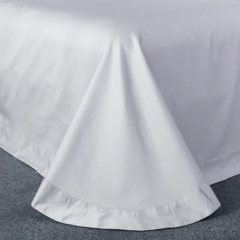 Grey flat sheet spread over a bed with a neat hem