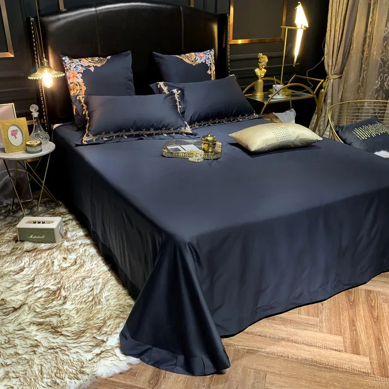 Plain navy flat sheet on a bed with embroidered pillowcases