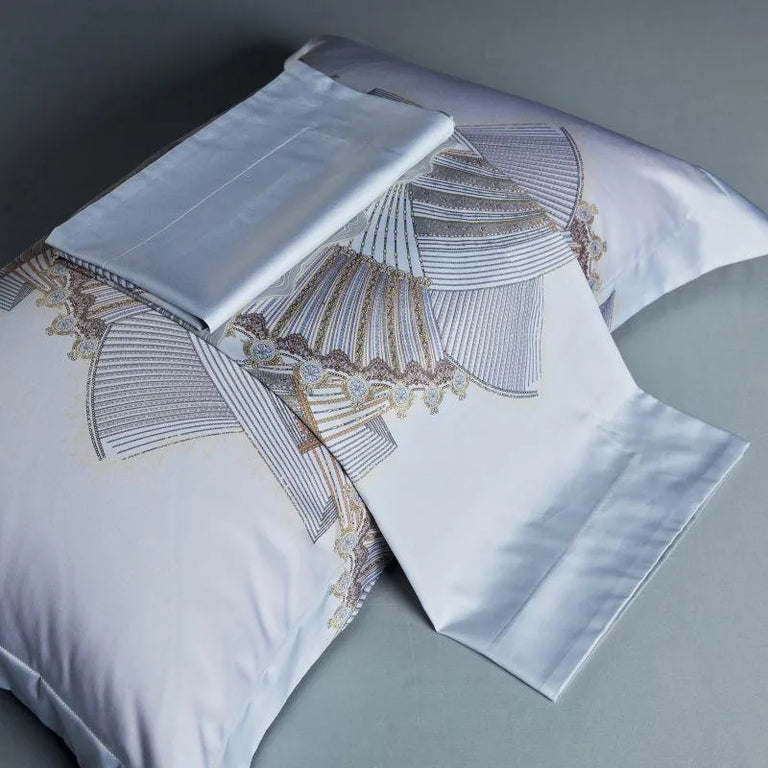 Folded silver blue sheet beside printed pillowcases