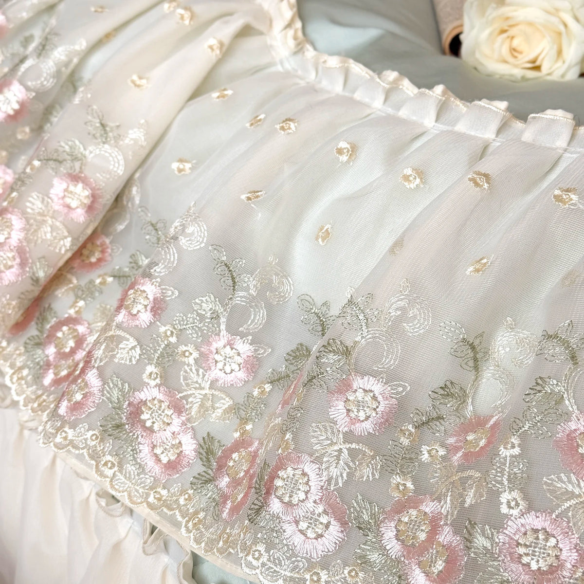 Close up of pink and green embroidered flowers on cream lace
